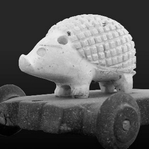 a little carved hedgehog in white stone, with short legs, a perky nose, and an engraved grid pattern representing the spines. It's standing on a dark stone cart with wheels.